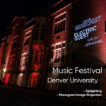 Nighttime brick university building lit in red, with a wall projection announcing a music festival and artists.