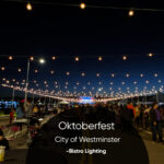 Night scene at Oktoberfest in Westminster with string lights overhead and a crowded outdoor dining area under Bistro Lighting.
